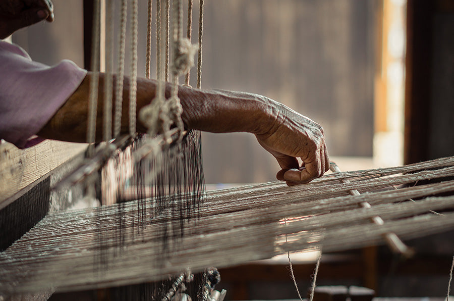 Person weaving with a traditional loom in a warm-toned setting