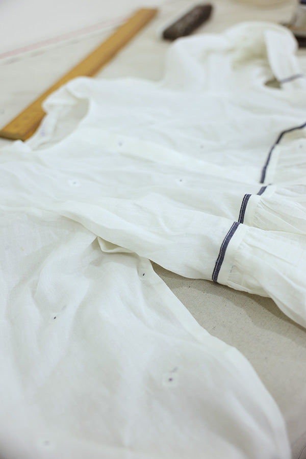 A white lightweight cotton top with contrasting piping laid on a surface