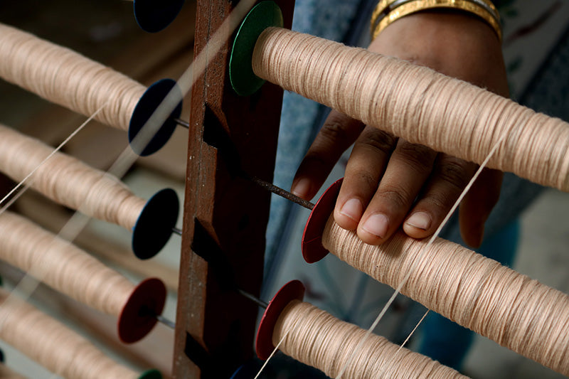 Hand holding a spool of thread on a traditional loom.