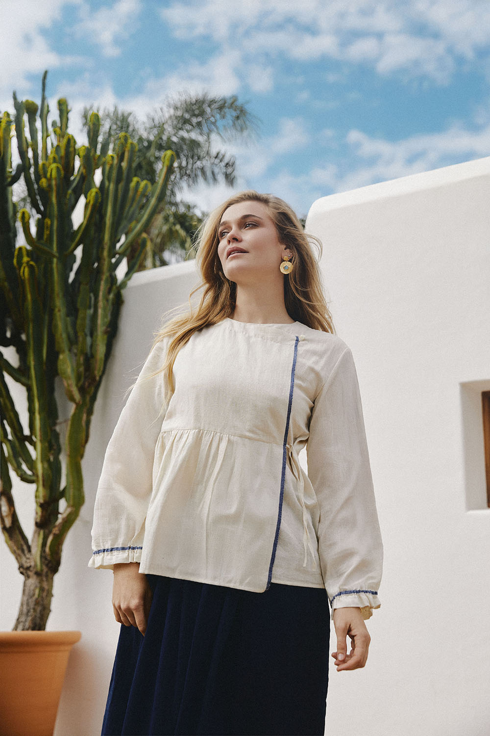Model standing outdoors wearing Morning Fold Wrap Top in off-white with a soft round neckline, gathered waist, and visible indigo selvedge.