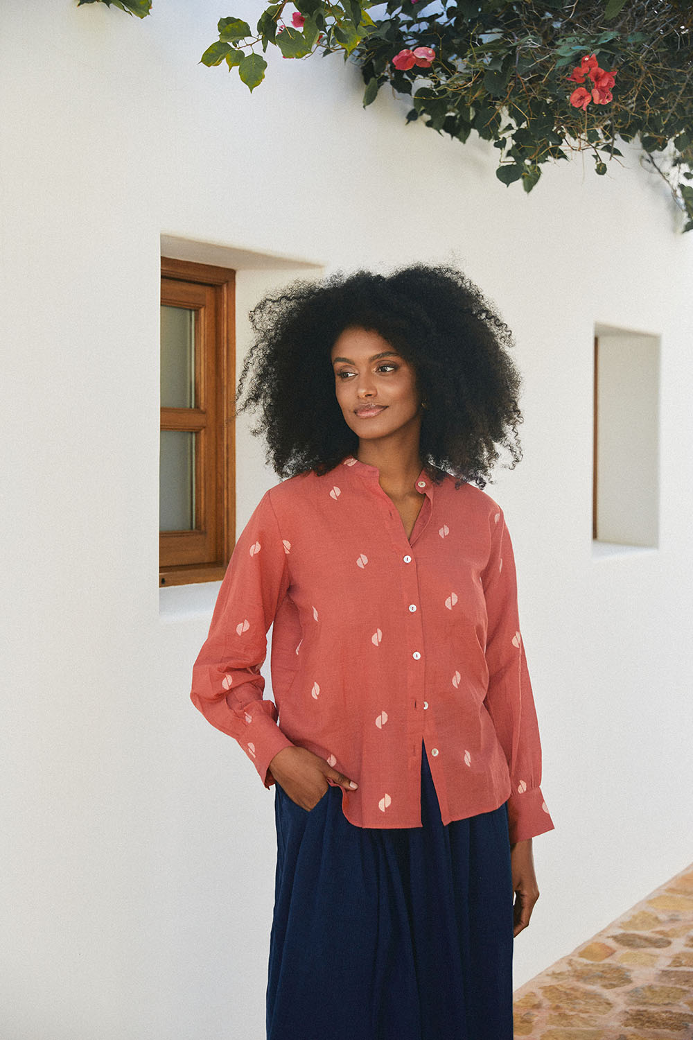 Model in the Sienna Moon Shirt in rust tone with subtle motifs, paired with a navy skirt, standing by a white wall.