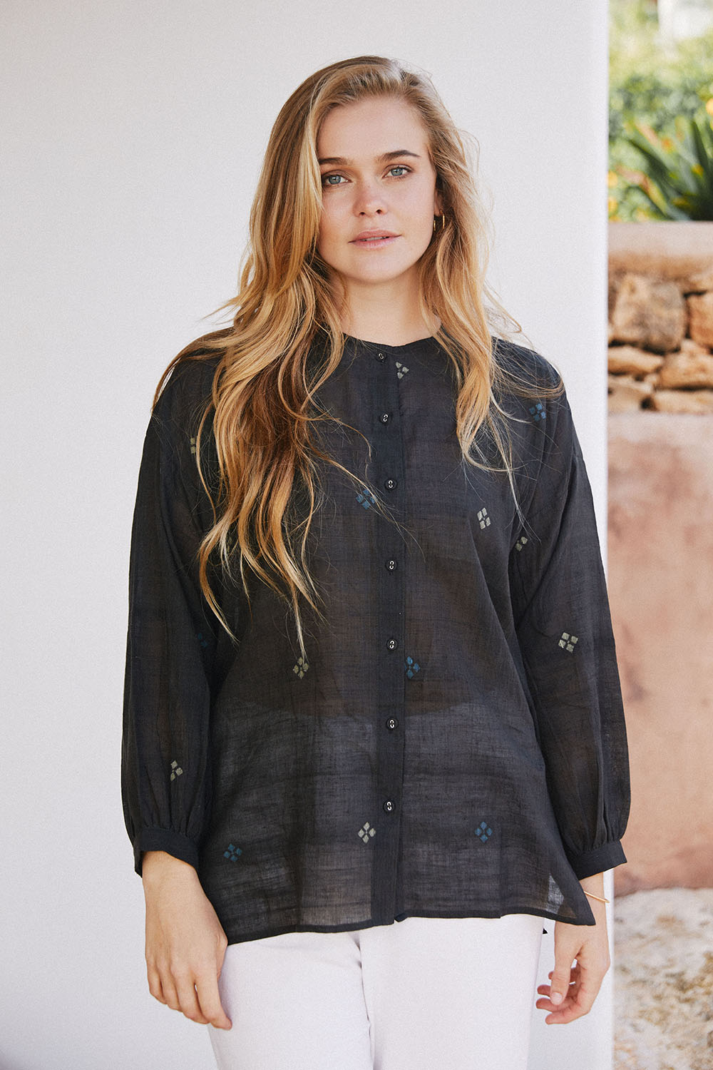 Model standing outdoors wearing Midnight Black Oversized Shirt with diamond motifs and a band collar, paired with white pants.