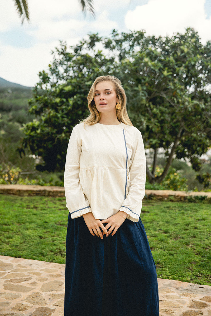 Model wearing the Morning Fold Wrap Top paired with the Indigo Dream Skirt, standing outdoors on a stone path with greenery in the background.