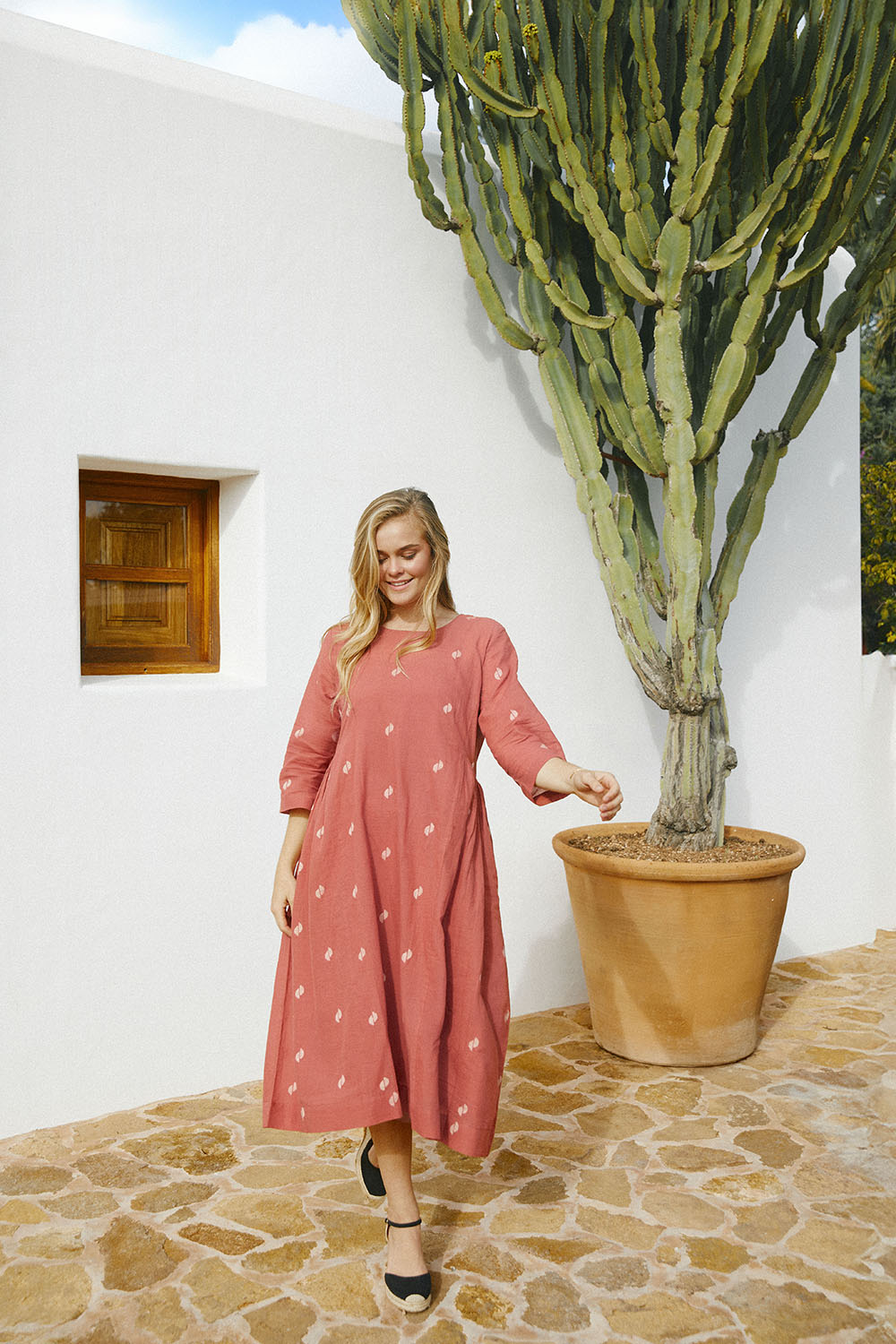 A person standing near a large cactus, wearing the rust-colored, long-sleeved, Sienna Moon Side Flared Dress with a round neckline.